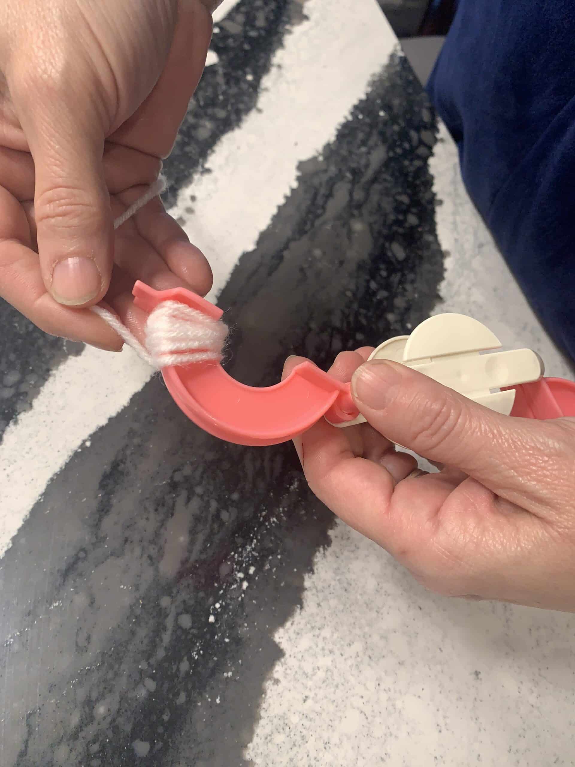 Winding white yarn onto a pom-pom maker.