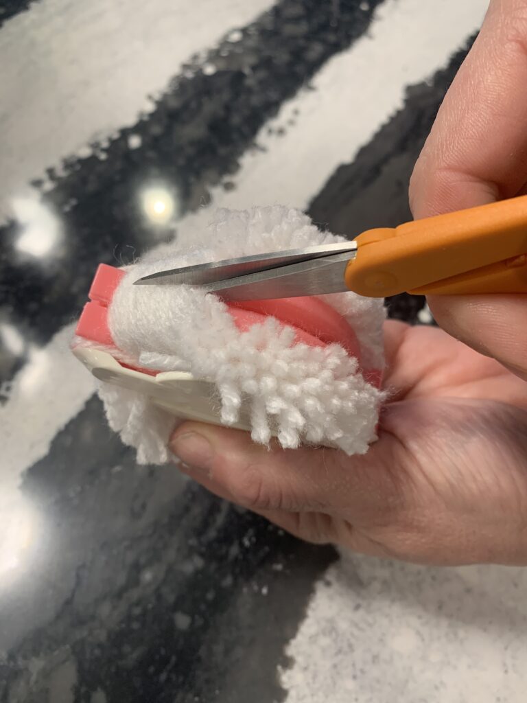 Scissors cutting the yarn on the pom-pom maker.