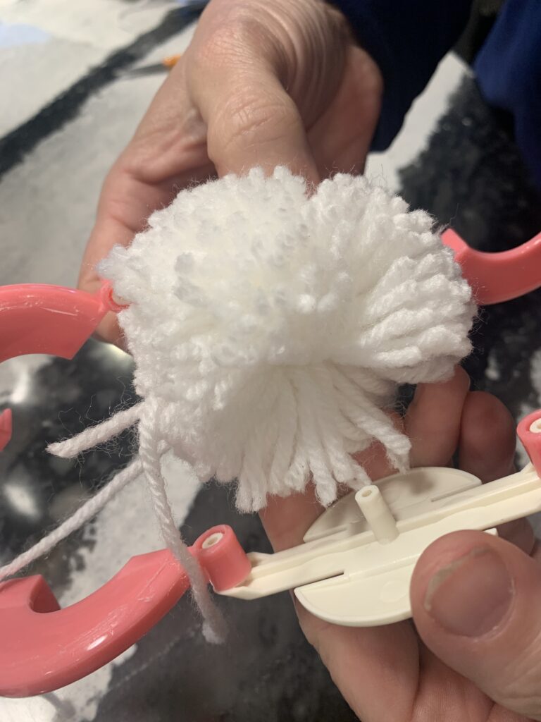 Removing the pom-pom maker to reveal the finished pom-pom.