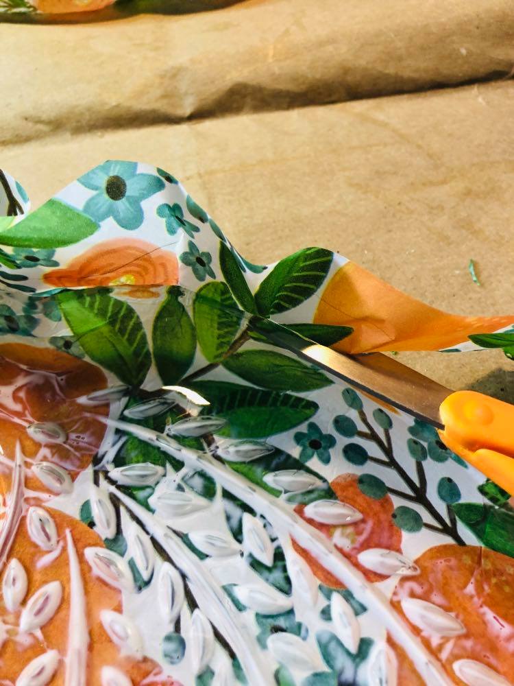 Trimming the excess tissue paper from the glass snack plate with scissors.