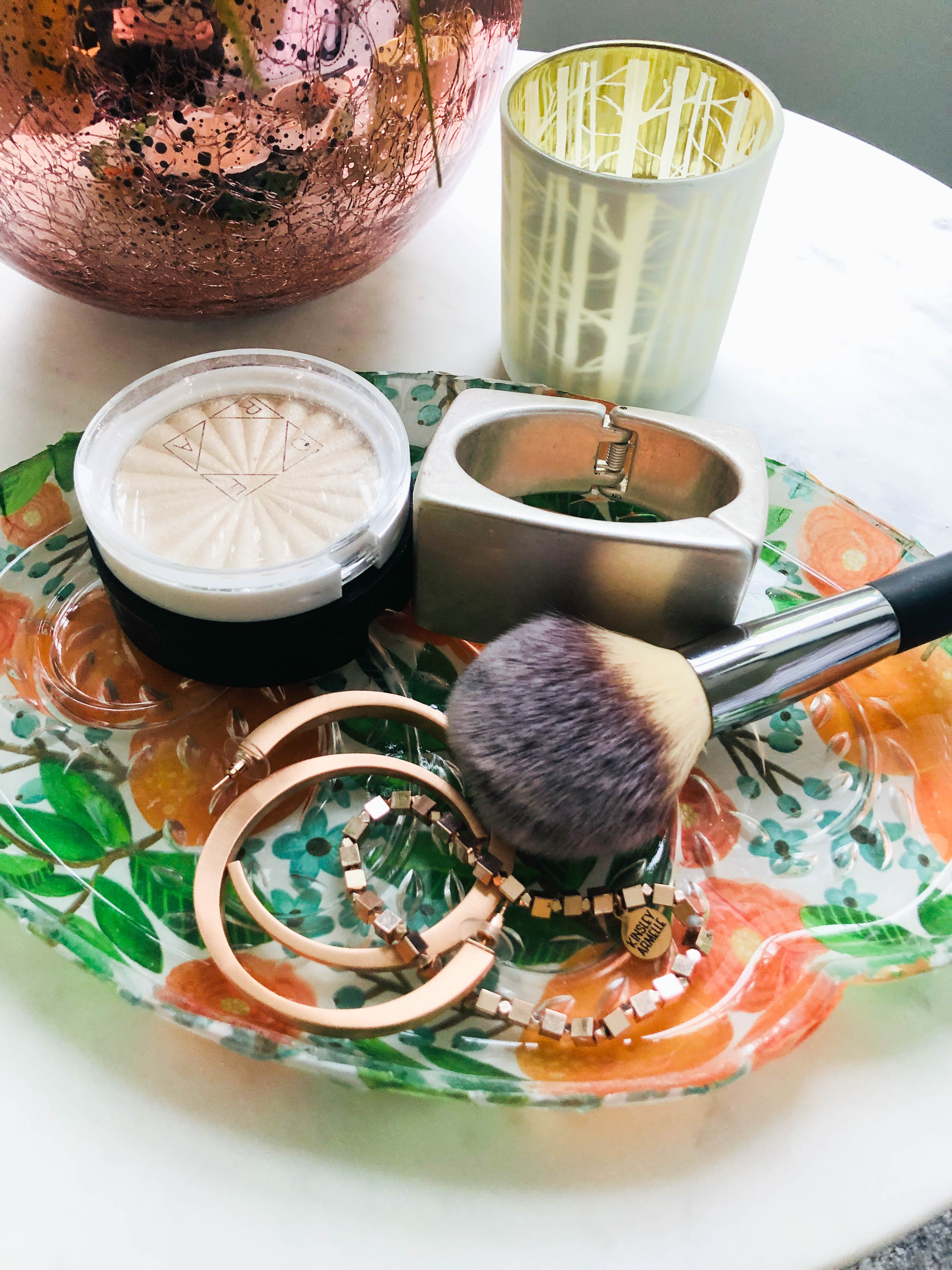 Jewelry and makeup brushes sitting on a completed glass snack plate.