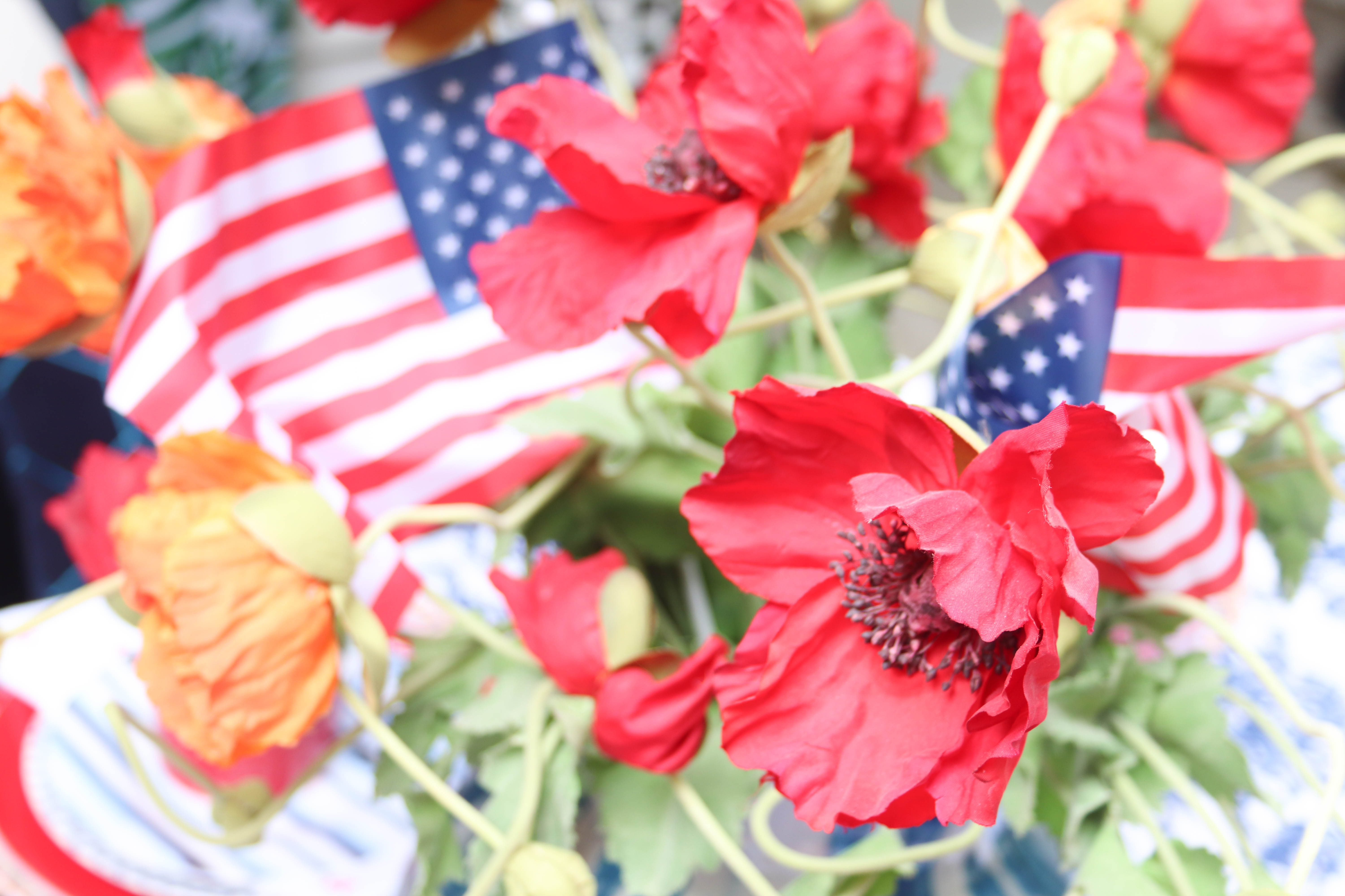 Faux red poppies and small American flags in a centerpiece display for the Memorial Day Table.