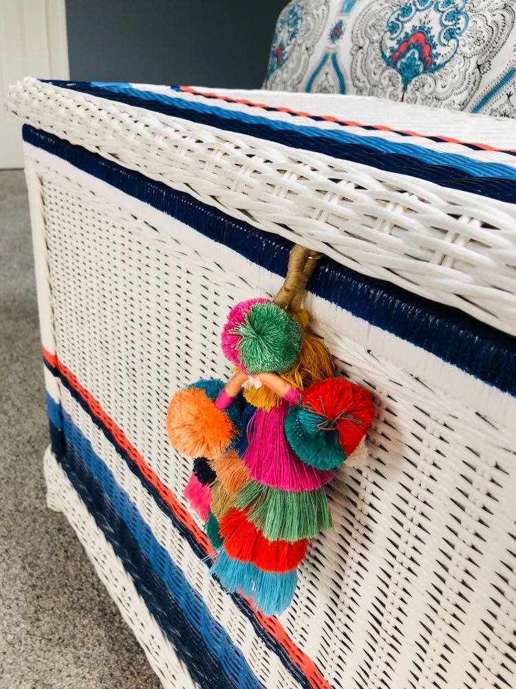 A brightly colored tassel charm used as a lid handle on a wicker chest.