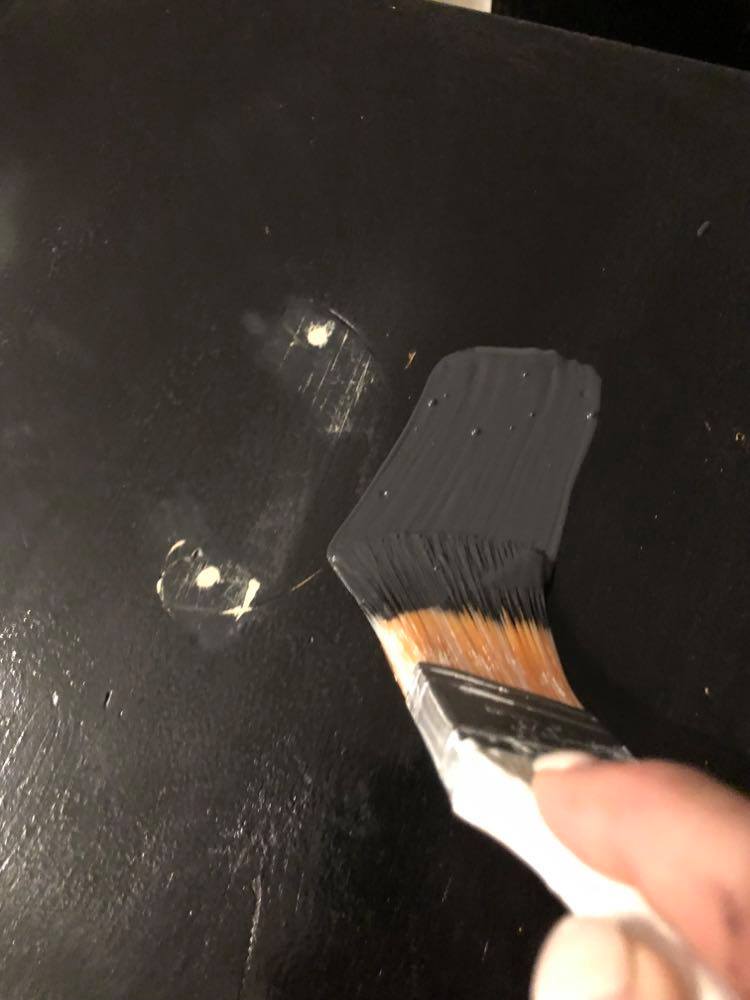 A paintbrush applying black paint to the file cabinet in this diy project.