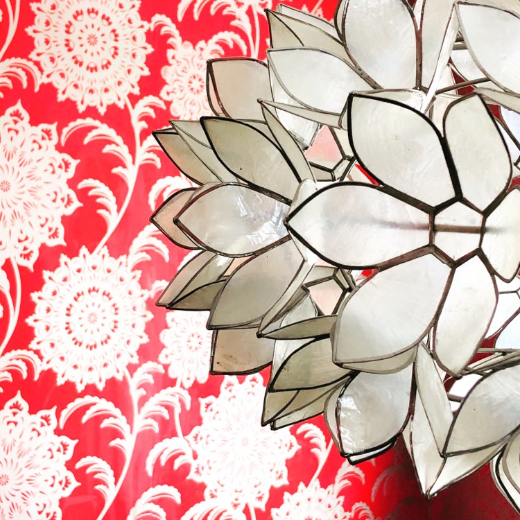 Coral and gold wallpaper behind a dining room light fixture.