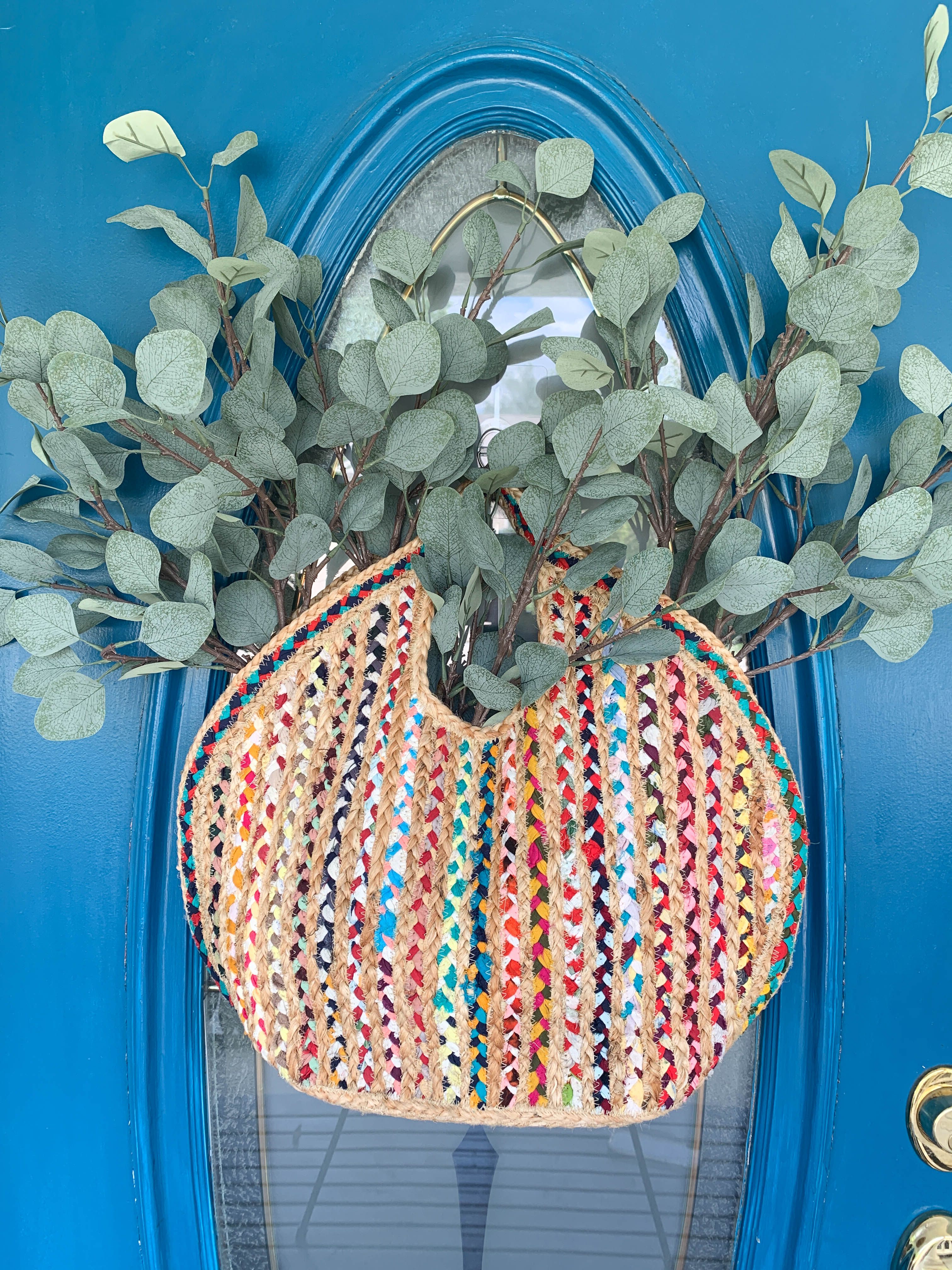 A woven handbag holding faux eucalyptus stems.