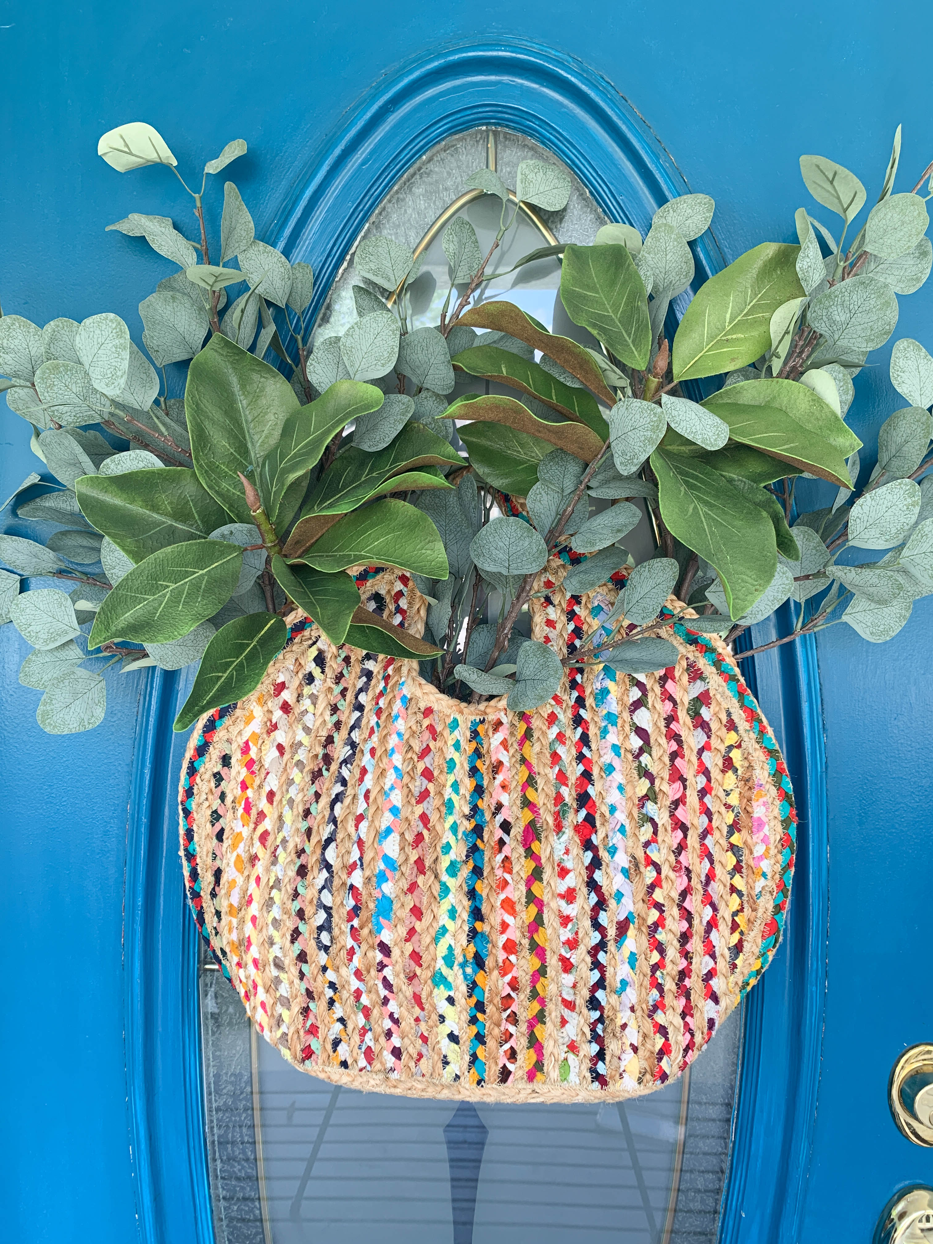 A woven purse holding magnolia leaf branches and hanging on a front door as decor.