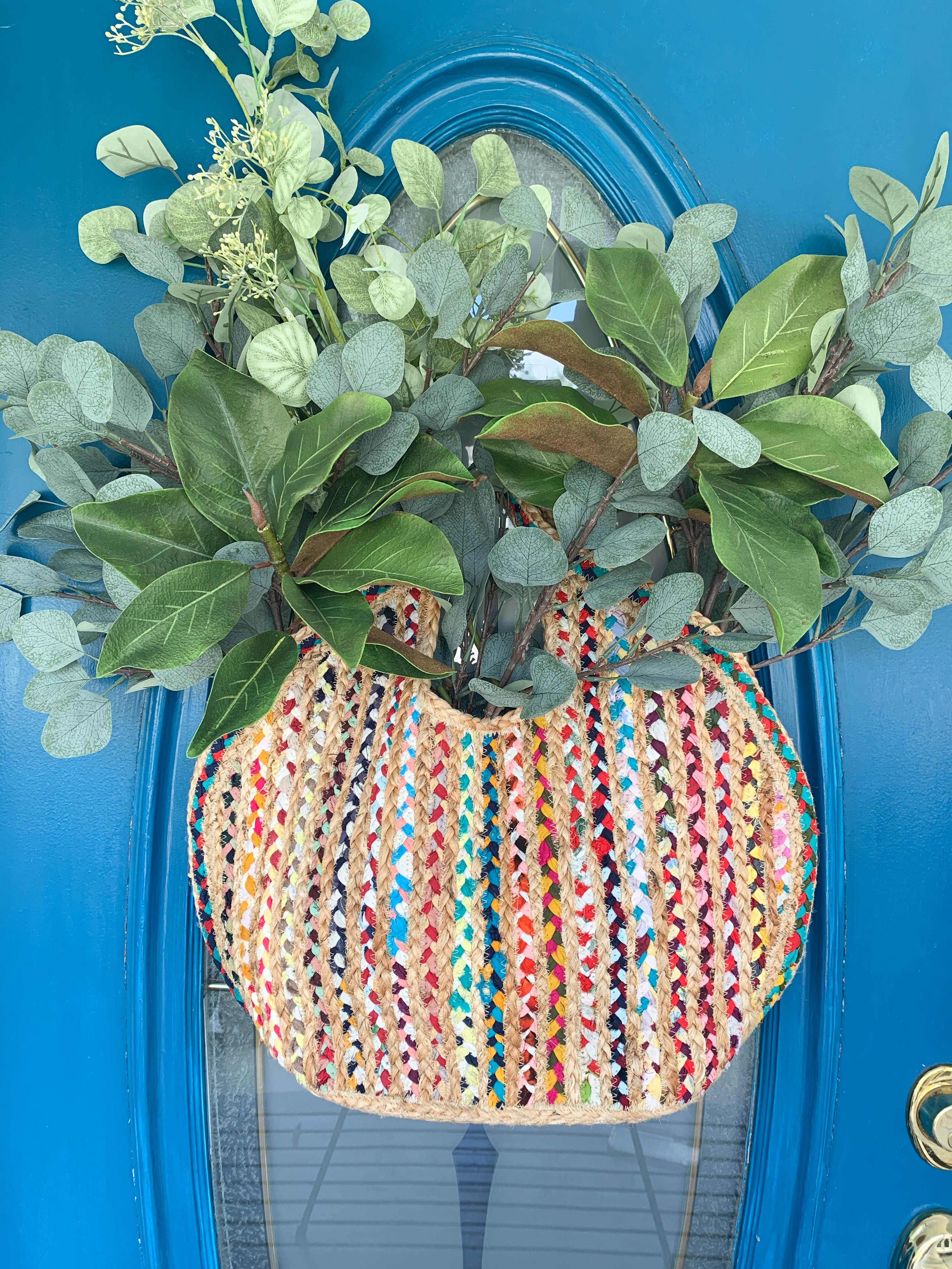 A multi-colored handbag holding various faux greenery as front door decoration.