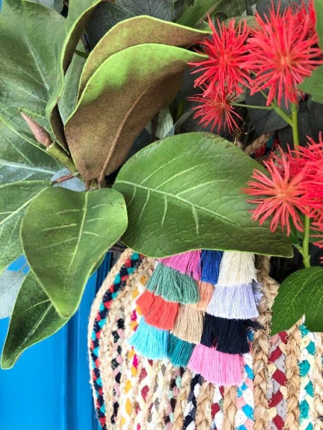 A woven handbag holding faux greenery and flowers and hanging on a front door as decor.