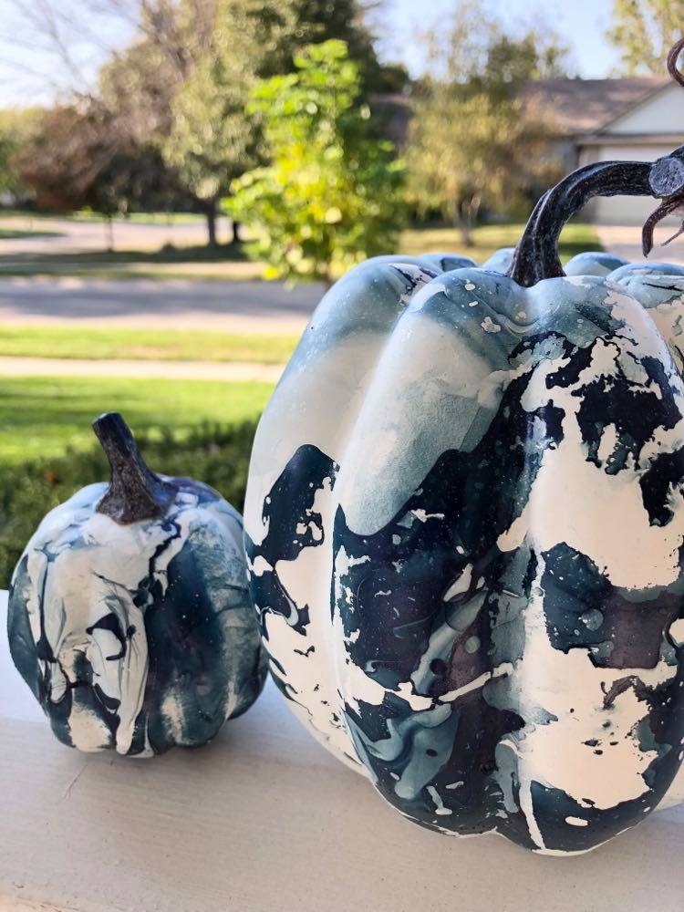 Painted abstract pumpkins displayed on a porch railing outdoors on a sunny day.