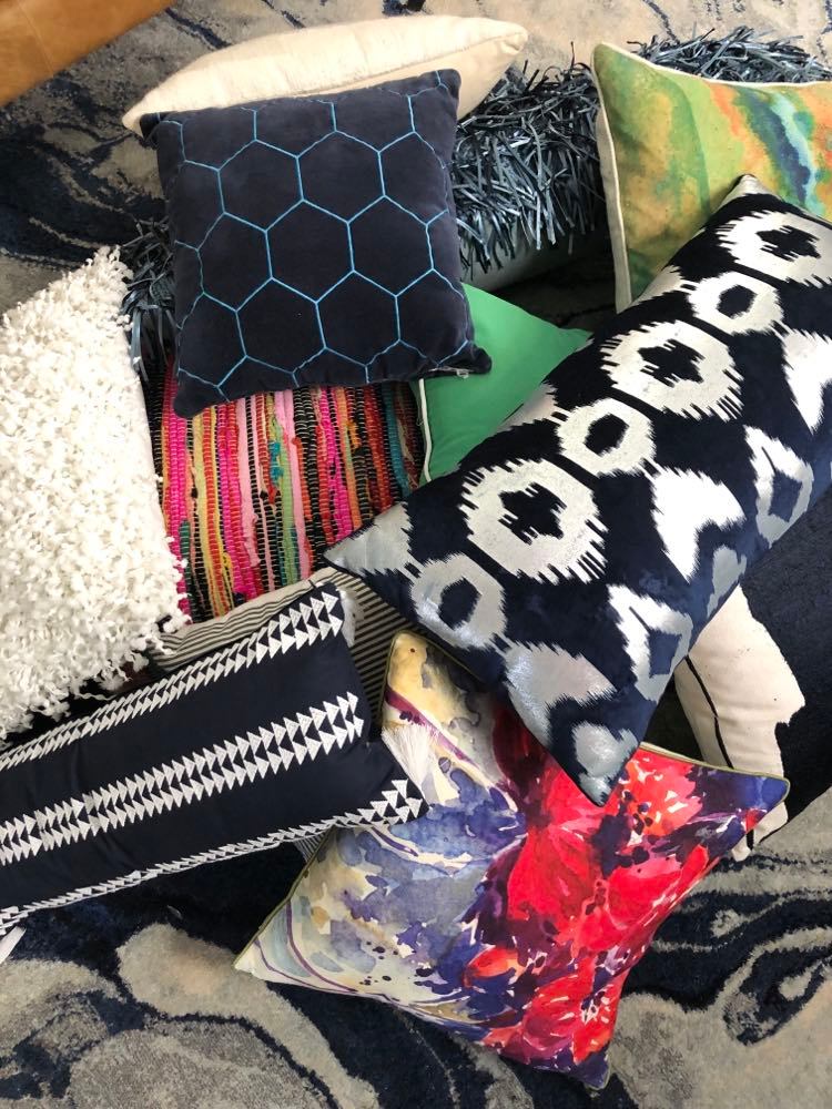 A pile of pillows in a variety of shapes, colors, and textures.