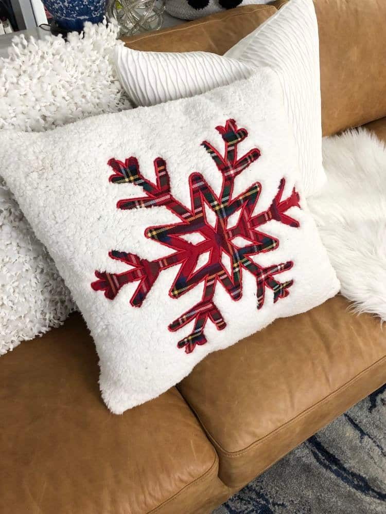 A white pillow with a red plaid snowflake in the center.