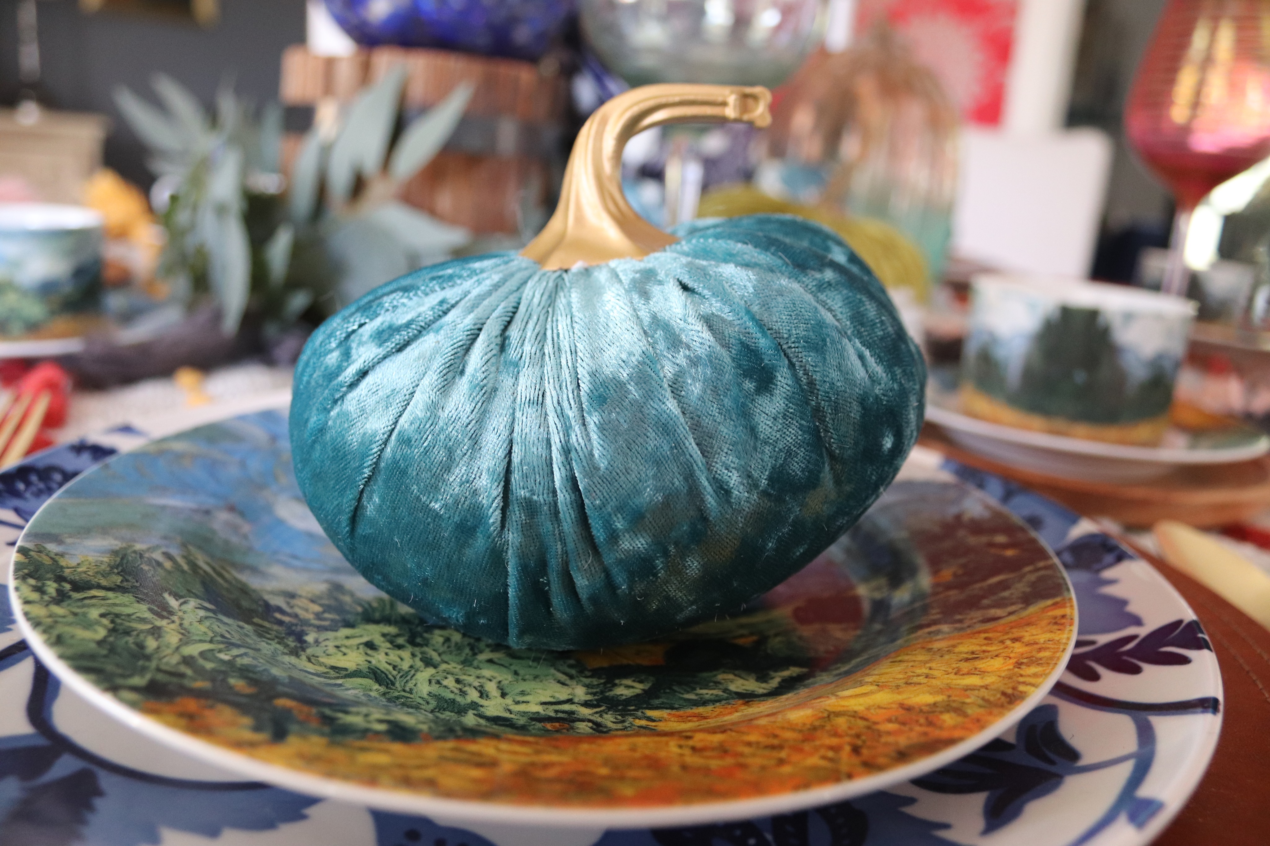 A teal colored velvet pumpkin sits on a place setting on this colorful Thanksgiving table.