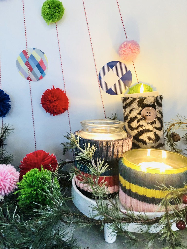 Jar candles wrapped in DIY sweater sleeves and displayed in front of the wall Christmas tree.