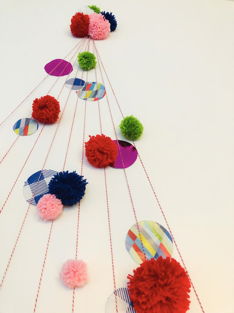 Fluffy pom poms in bright colors attached to the wall to create a flat wall Christmas tree.