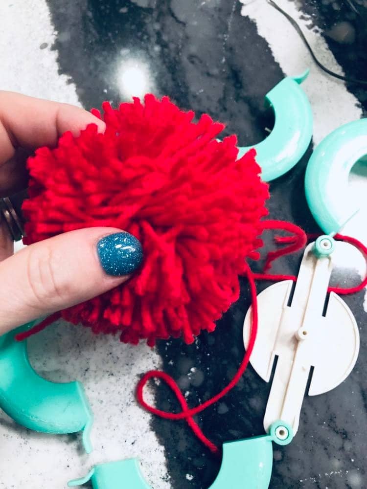 A newly created red pom pom ball with the pom pom maker.