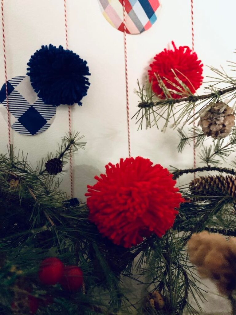 Patterned paper circles and red pom pom balls attached to the strings of the  DIY wall Christmas tree.