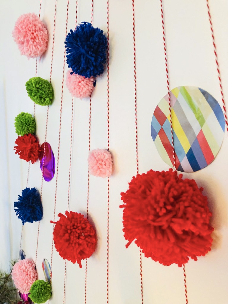 A bright DIY wall Christmas tree with multi colored pom poms and festive paper.