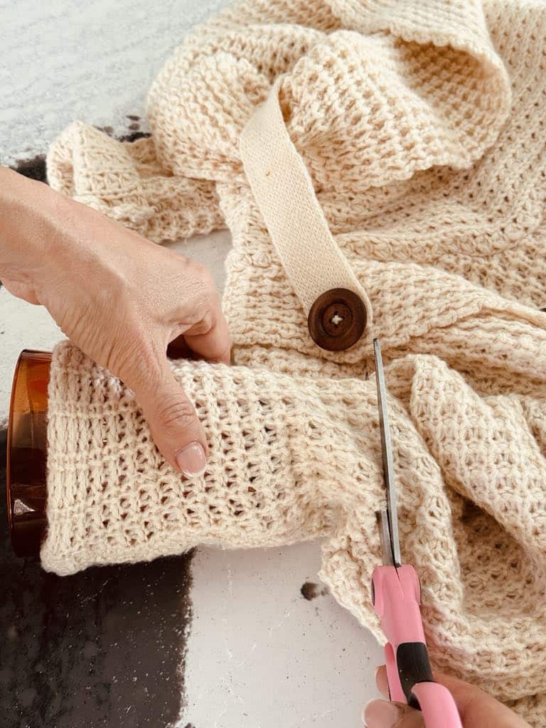 Cutting a sweater sleeve an inch longer than the candle jar.
