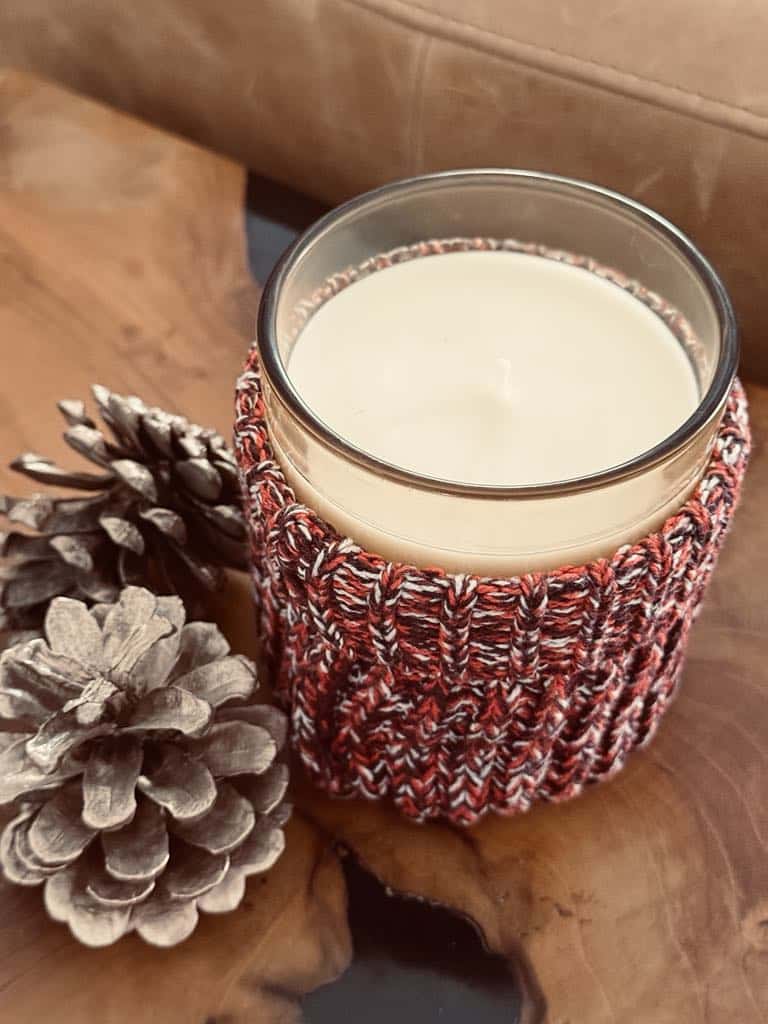 A candle jar with a cozy sweater wrap in a russet color.