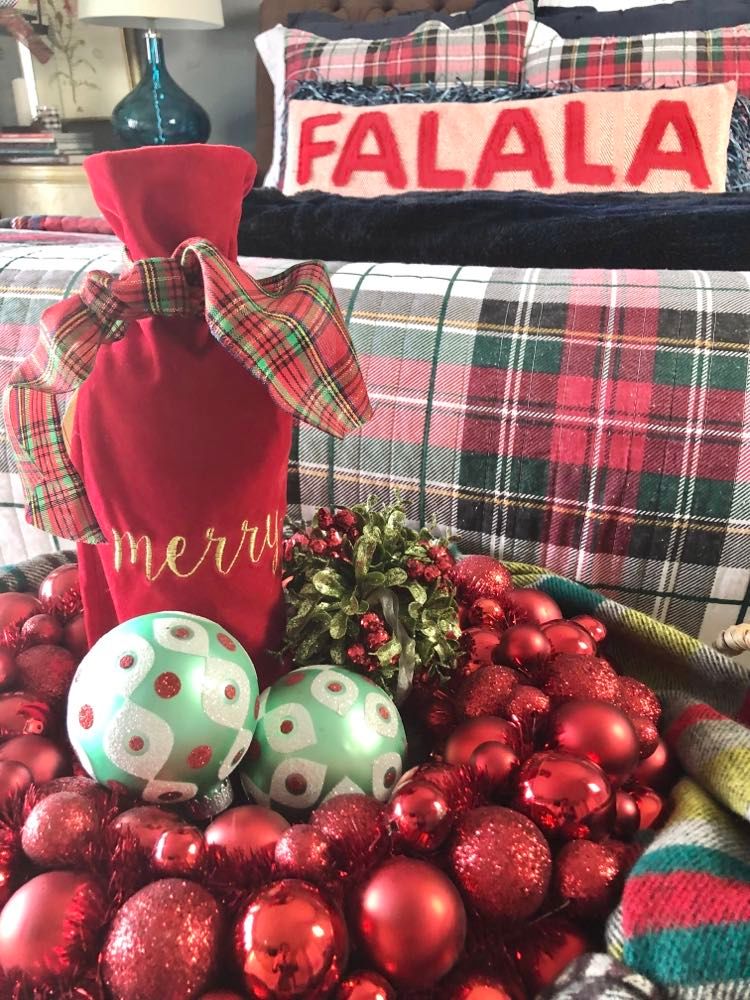 A red wine bottle bottle bag nestled amidst a red ornament wreath and plaid scarf.