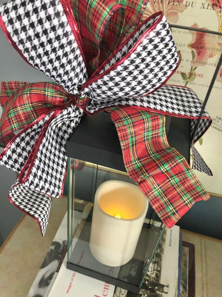 A black lantern with a double plaid tidings Christmas bow.