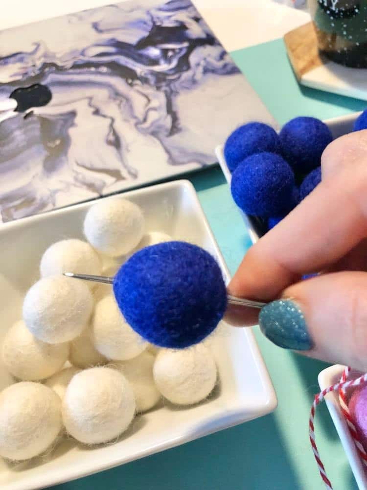 Large eye needle threading a cobalt blue felted wool ball.