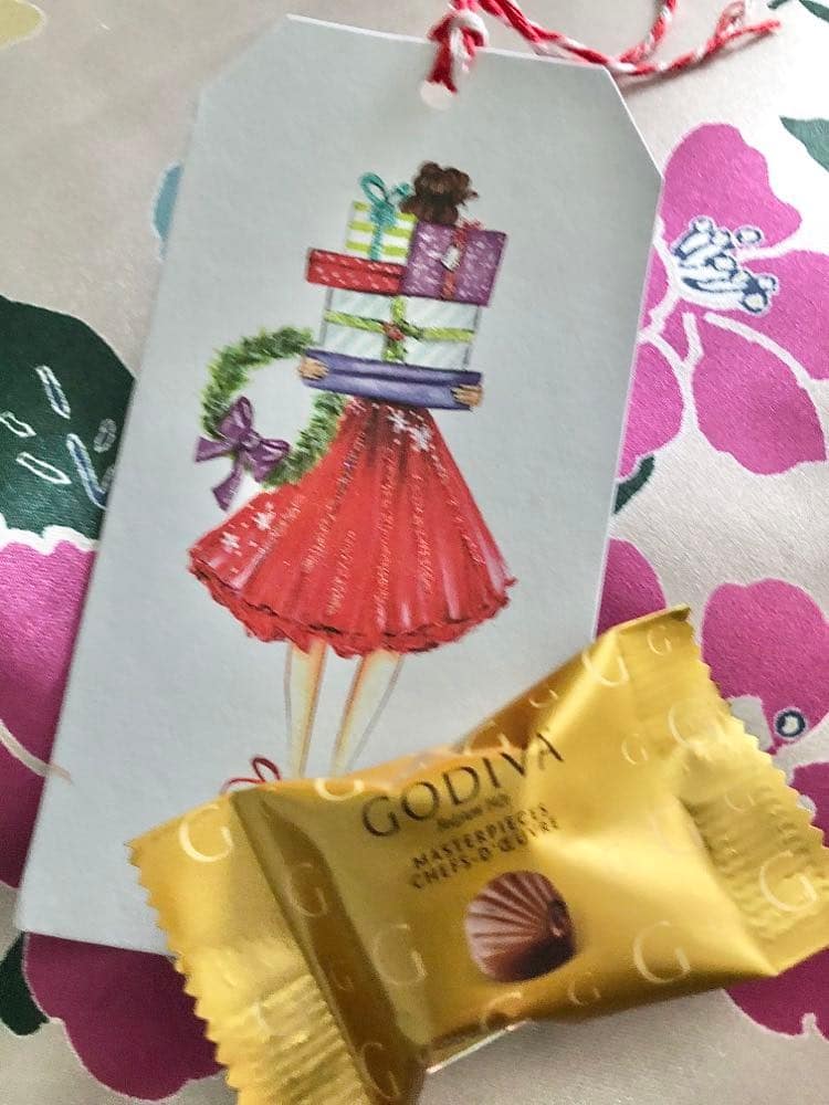 A foil wrapped chocolate with a Christmas gift tag placed on top of a bedroom pillow to welcome guests.