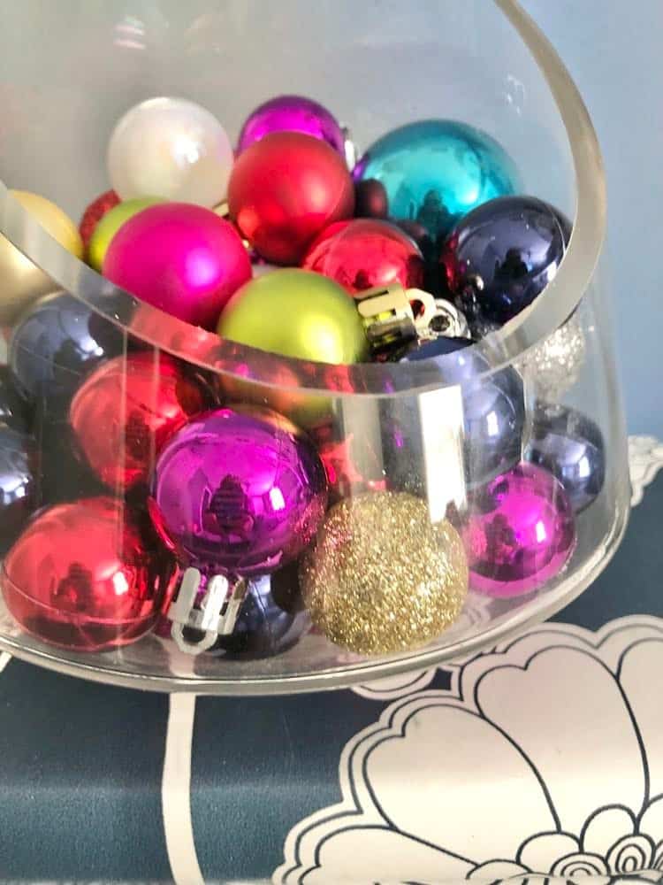A glass bowl full of small ornament balls to welcome guests.