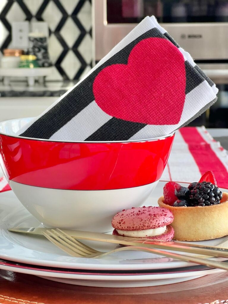 A tea towel with a heart on it placed diagonally in a red and white stripe bowl.