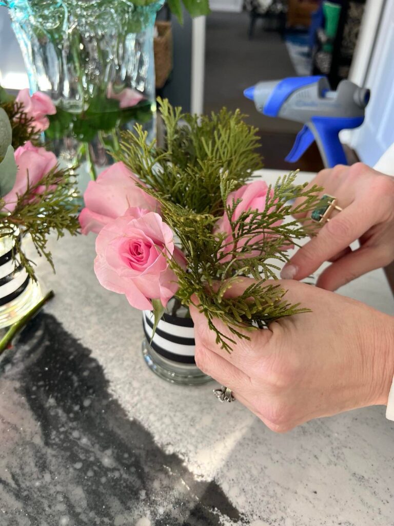 Adding greenery to the small flower arrangement.