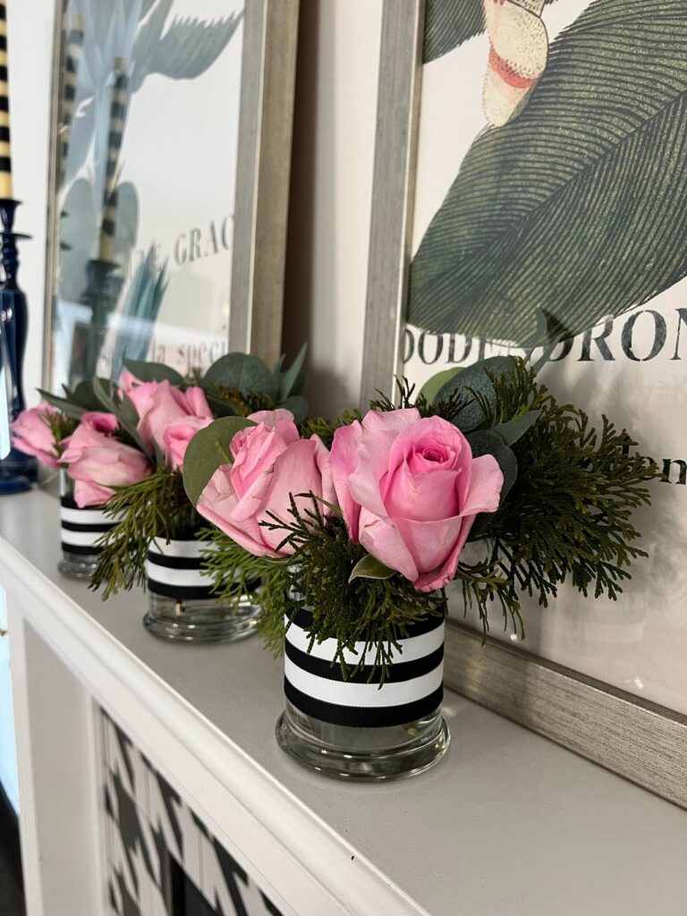 Pink roses in small glass vases decorated with black and white striped ribbon.