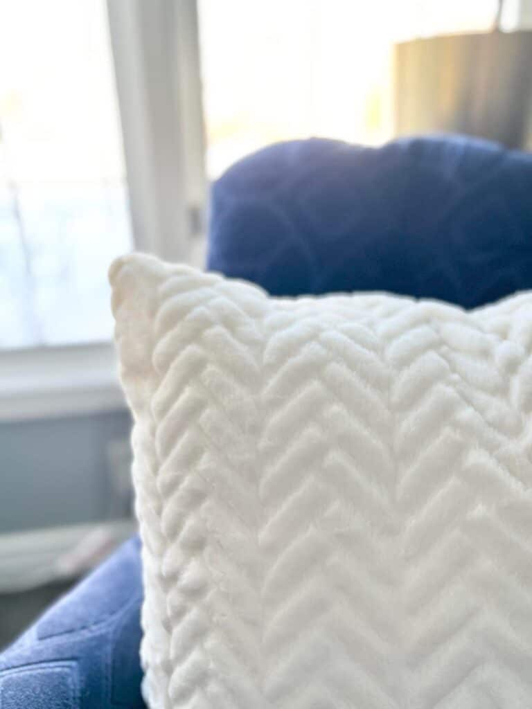A white fluffy pillow sitting on a blue chair.