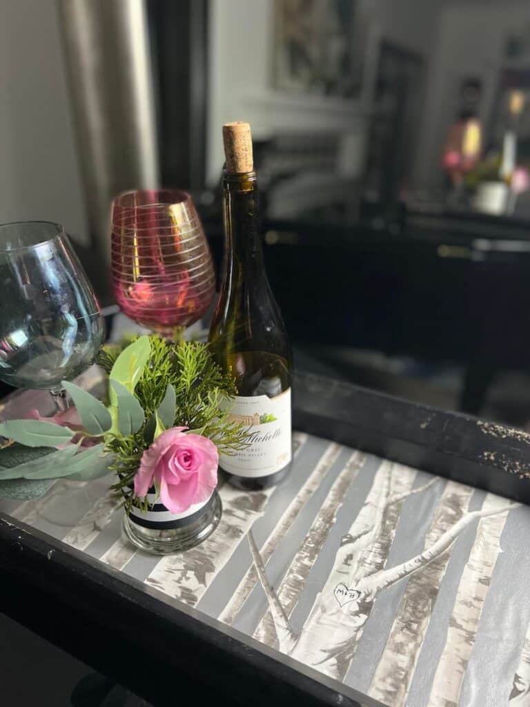 A wallpaper tray holding wine glasses, a wine bottle, and a pink rose.