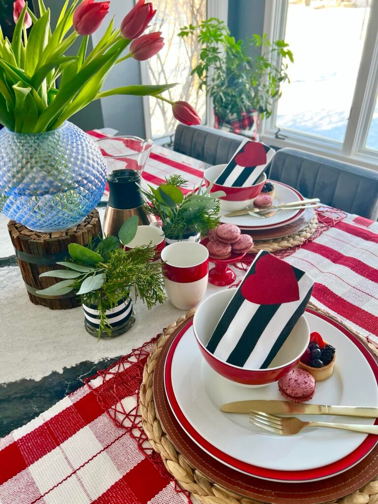 A Valentine table complete with layers of linens, bright red colors, and fresh red tuips.