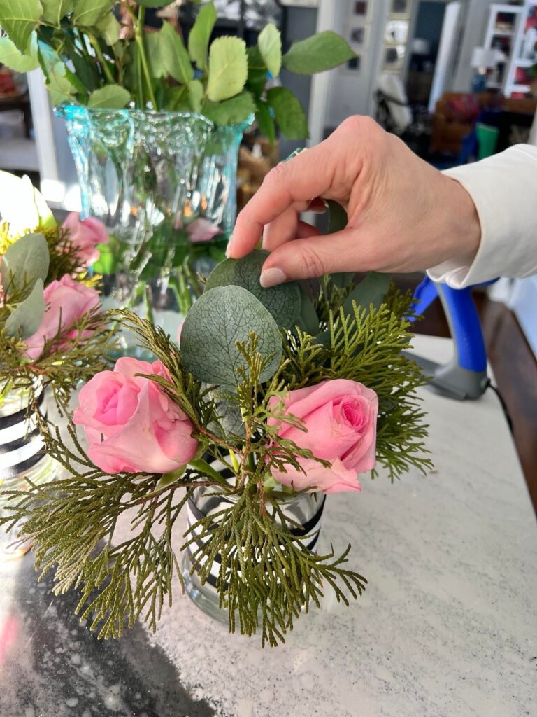 Adding faux greenery to the small flower arrangement.