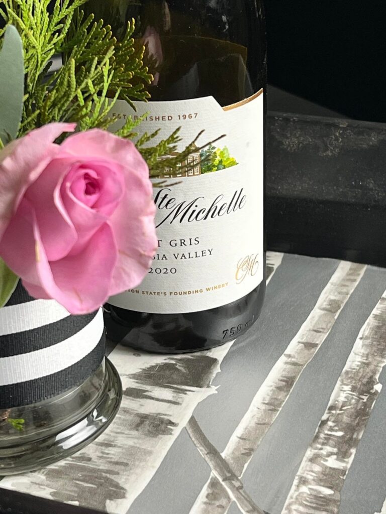 Close up of a wine bottle and pink rose on top of a wallpaper tray.