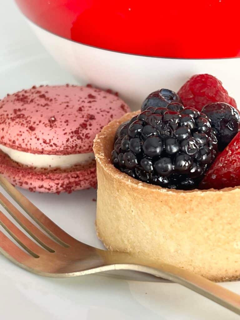 A pink macaron and a mini fruit tart with a gold fork.