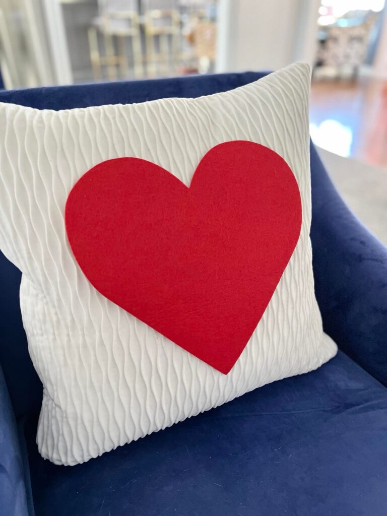 A red felt heart is placed on a white pillow for Valentine's Day home decor.
