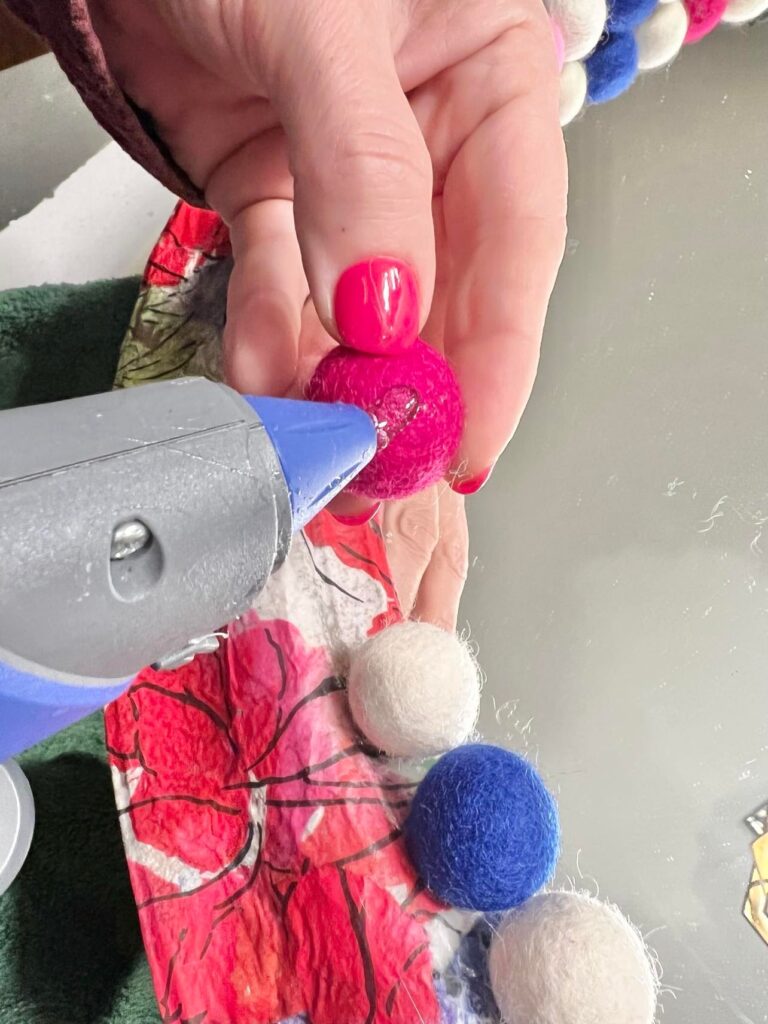 Applying glue to a wool felt ball using a glue gun.
