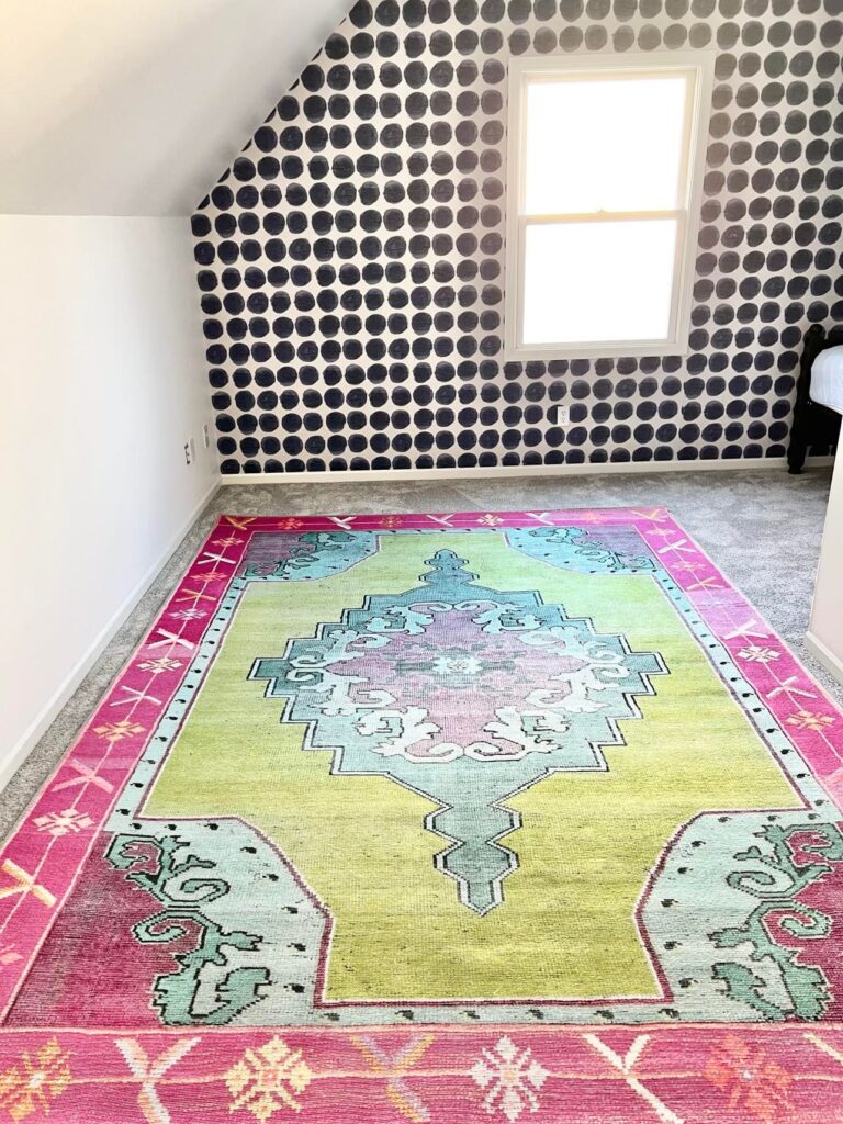 Stage one of creating a craft room is complete with painted walls and ceiling, wallpapered walls in blue dots, and a green, pink, and blue rug.