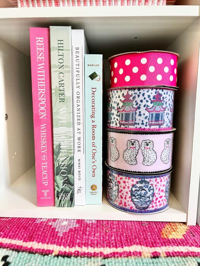 Craft room storage for home decor books and a stack of pink and white ribbon.