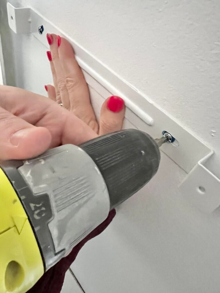 
Two sets of hands screwing the pegboards to the wall.