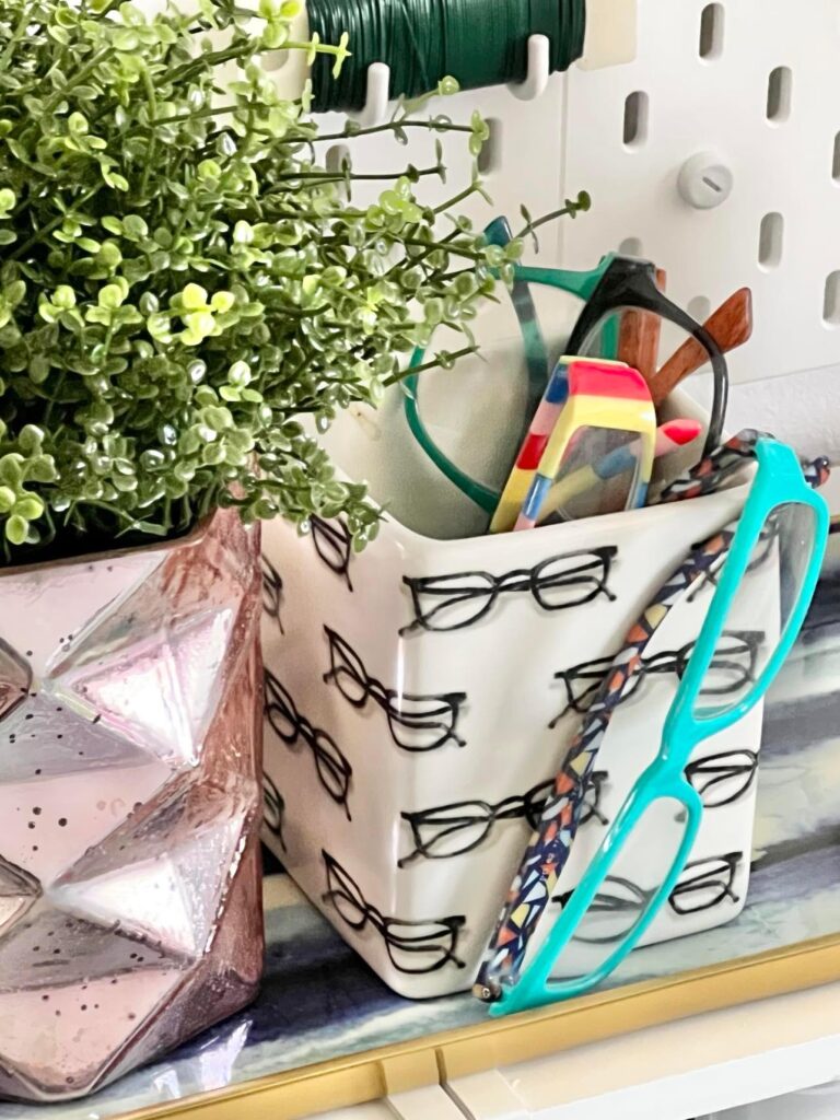 
A white vase holding several pairs of reading glasses.