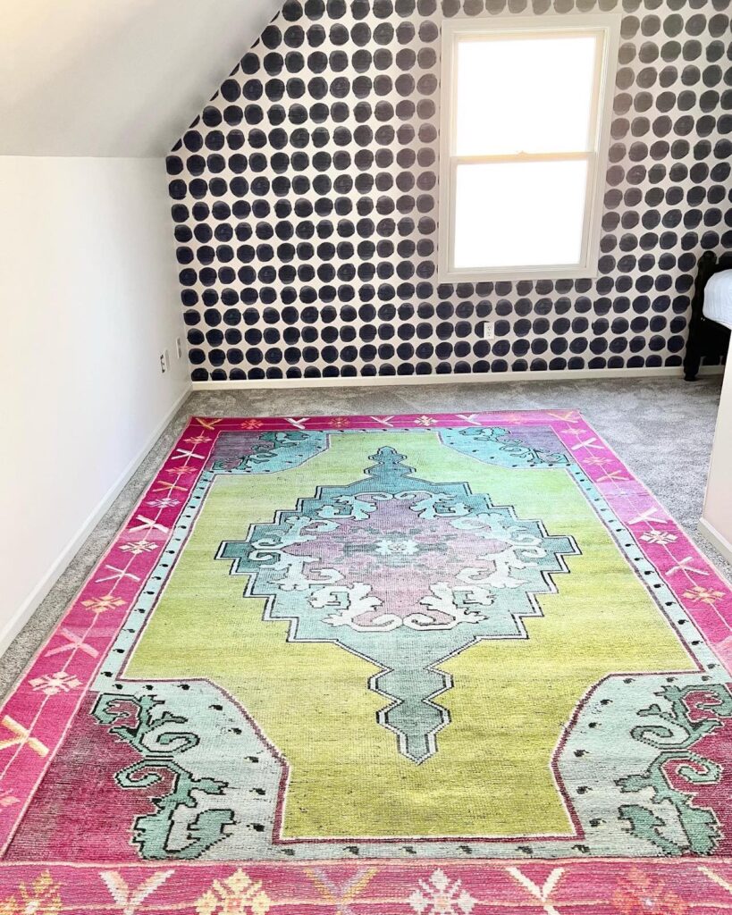 The craft room with the dot wallpaper installed and a pink, green, and blue rug on the floor.