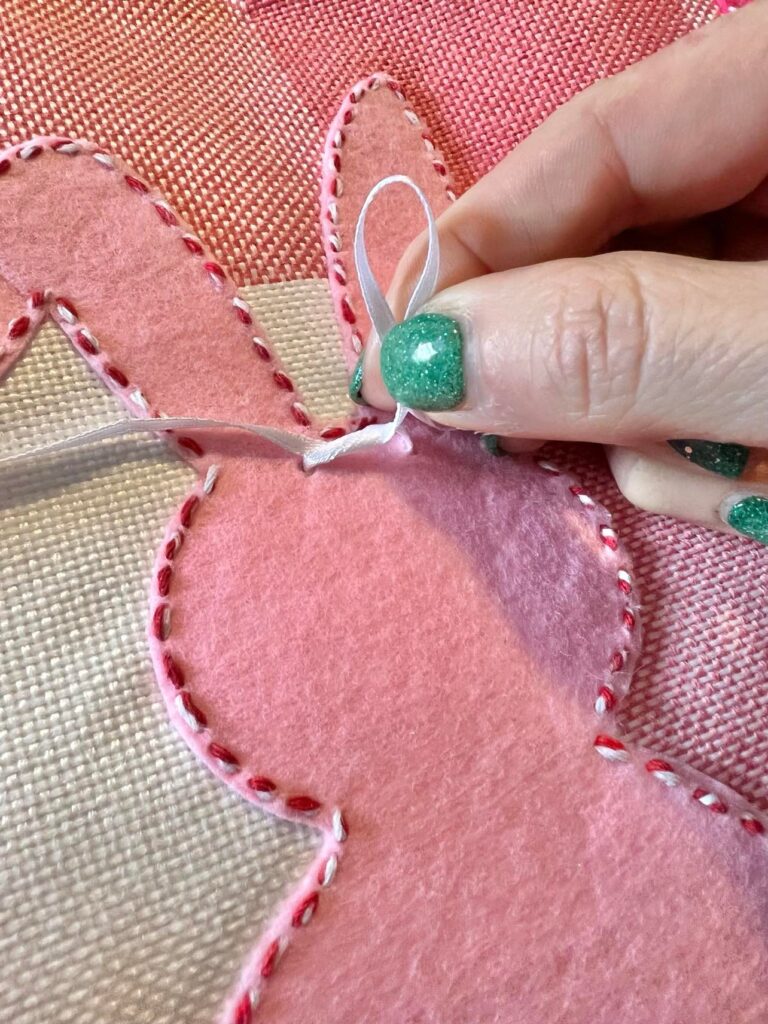 Adding a white bow to the top of the bunny on this DIY Easter bunny pillow.