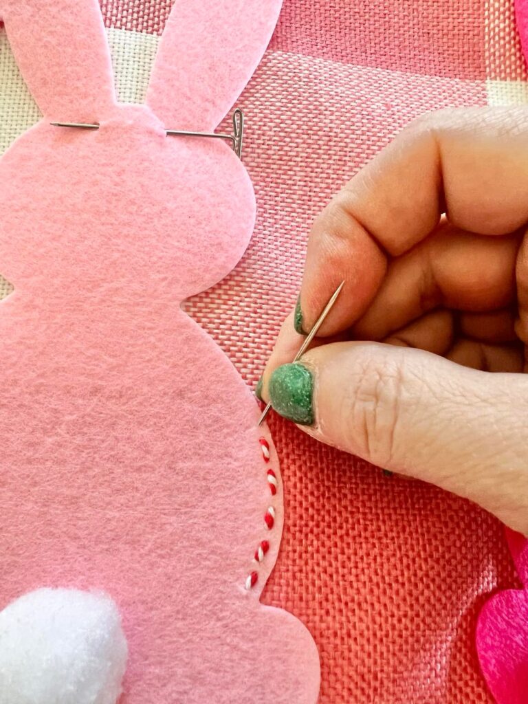 Missy using a needle to sew a straight stitch around the perimeter of the felt bunny.