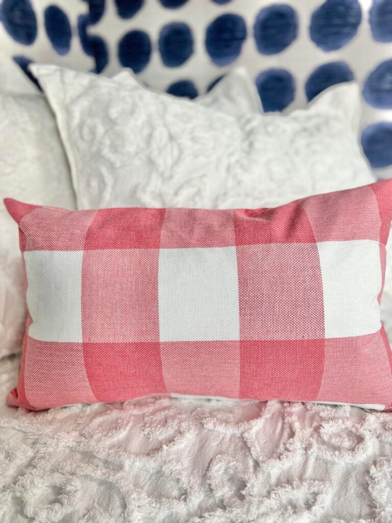 A pink buffalo check lumbar pillow sitting on a white bed coverlet.