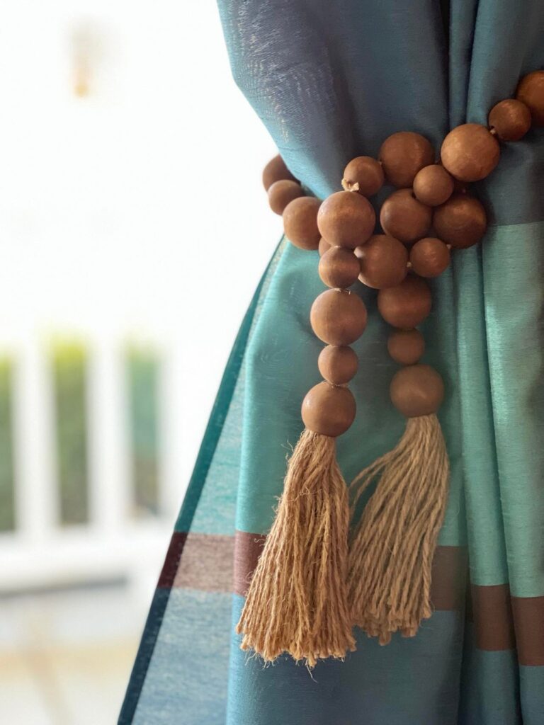 Blue and brown curtain panel held back by a brown wood bead garland to decorate a window.