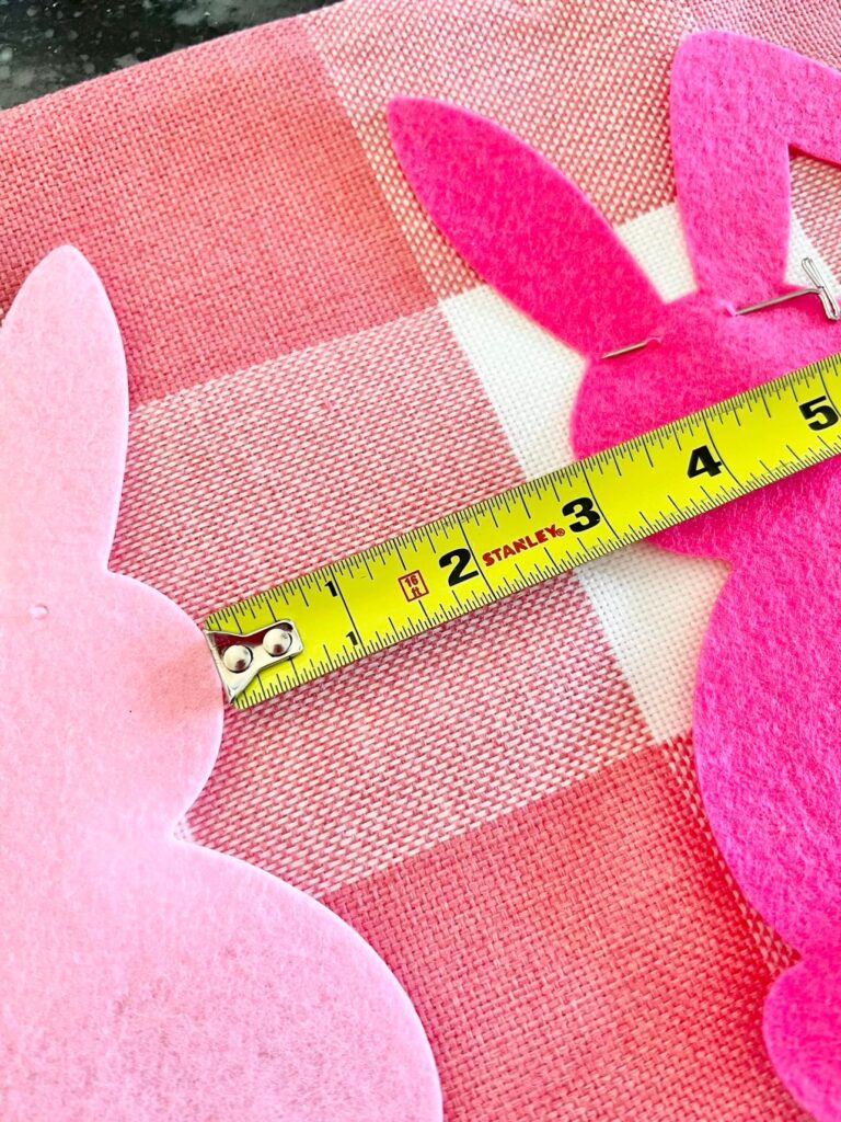 A tape measure laid on top of the DIY bunny pillow to ensure equal spacing between the felt bunnies.